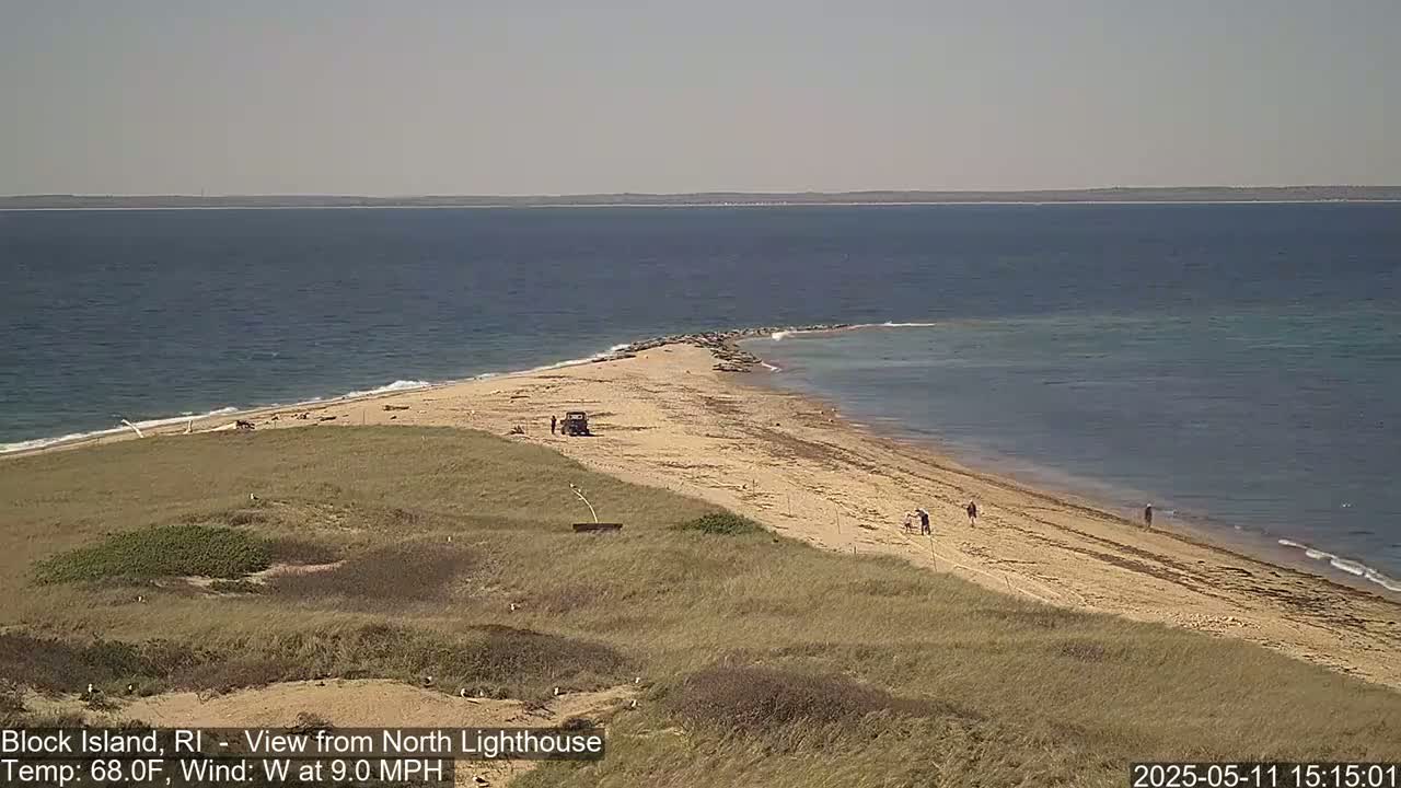 A sandy spit of land juts out into a calm ocean under a clear sky.