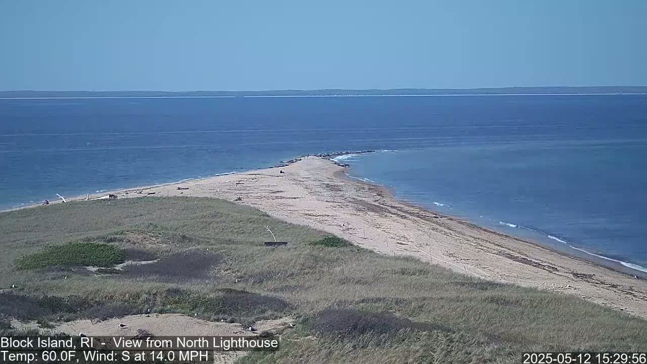 A sandy, curved shoreline extends into a calm blue ocean under a clear sky.