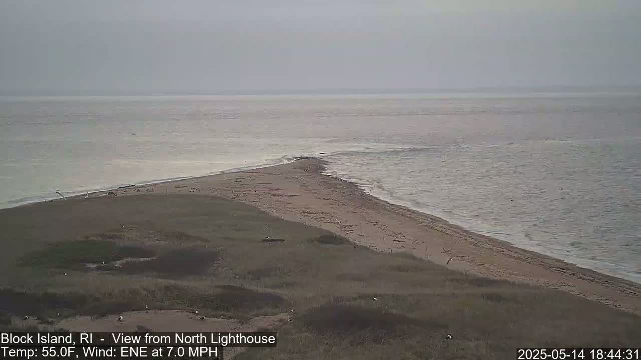 A sandy point of land juts into a calm, gray ocean under an overcast sky.