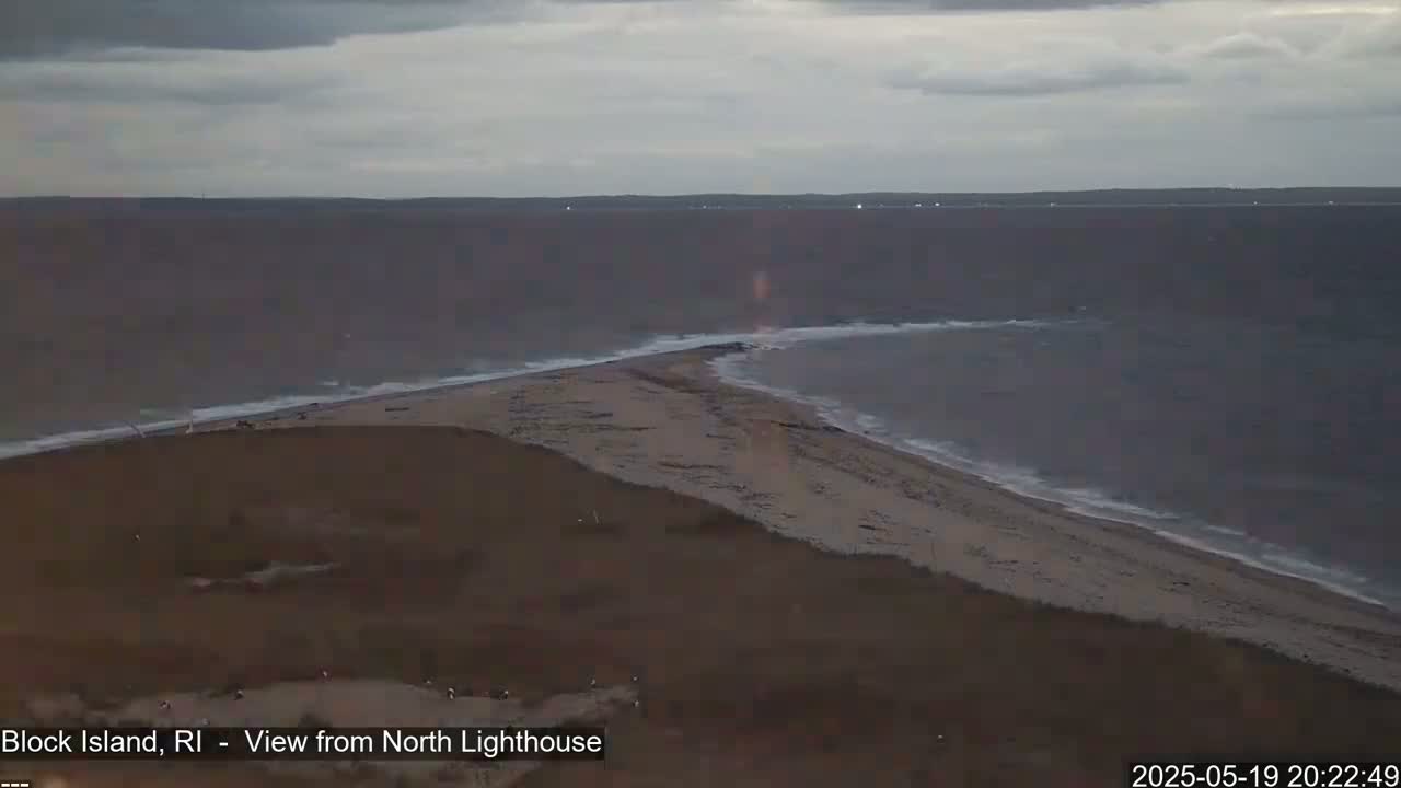 A sandy, narrow spit of land juts into a dark, wavy ocean under a cloudy sky.