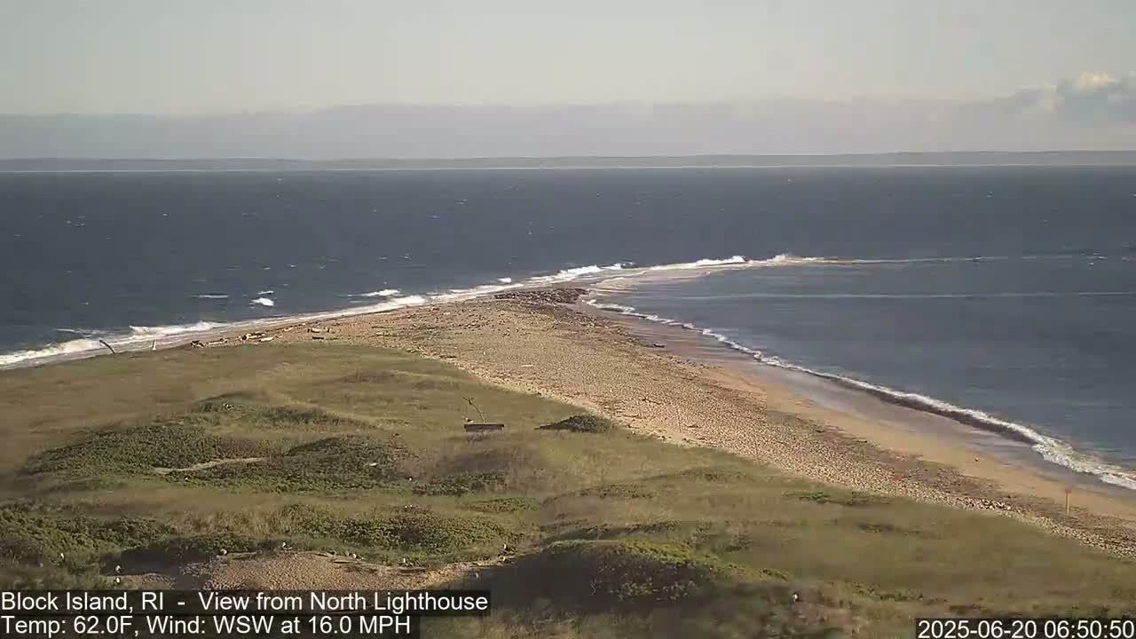 A sandy beach curves into a point where it meets a dark blue ocean with moderate waves under a mostly clear sky.