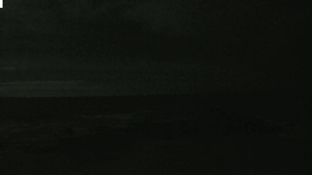A dark, nighttime scene shows a mostly obscured body of water under a dark sky.