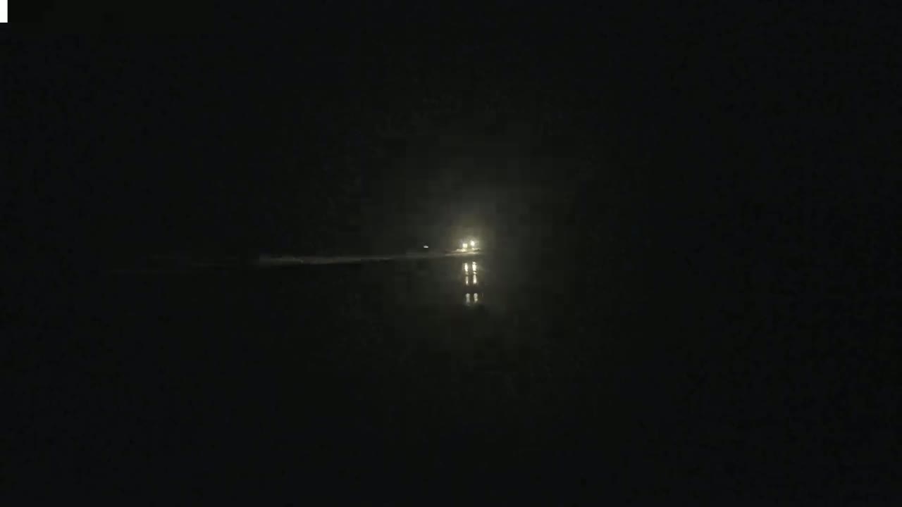 A vehicle's headlights are visible in the distance on a dark, possibly foggy, night.