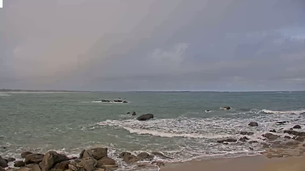 A rocky shoreline meets a moderately choppy sea under an overcast sky.
