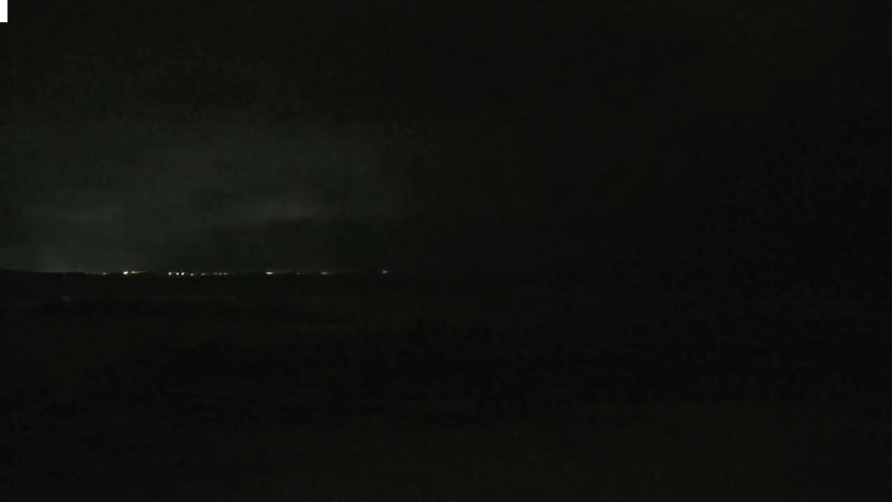 A dark, nighttime scene shows a faint line of lights on the horizon under a mostly cloudy sky.