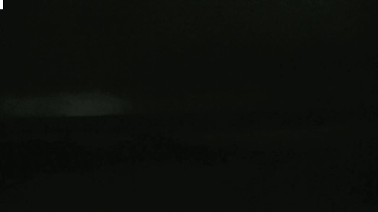 A low-light, nighttime image shows a faintly visible horizon line with a slightly brighter area in the distance, possibly fog or low clouds.