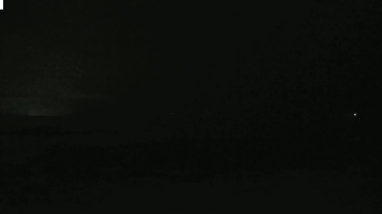 A dark, nighttime scene shows a faintly illuminated horizon under a mostly cloudy sky.