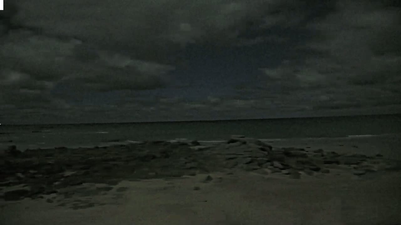 A dark, overcast sky hangs over a rocky shoreline and a calm, dark sea at night.