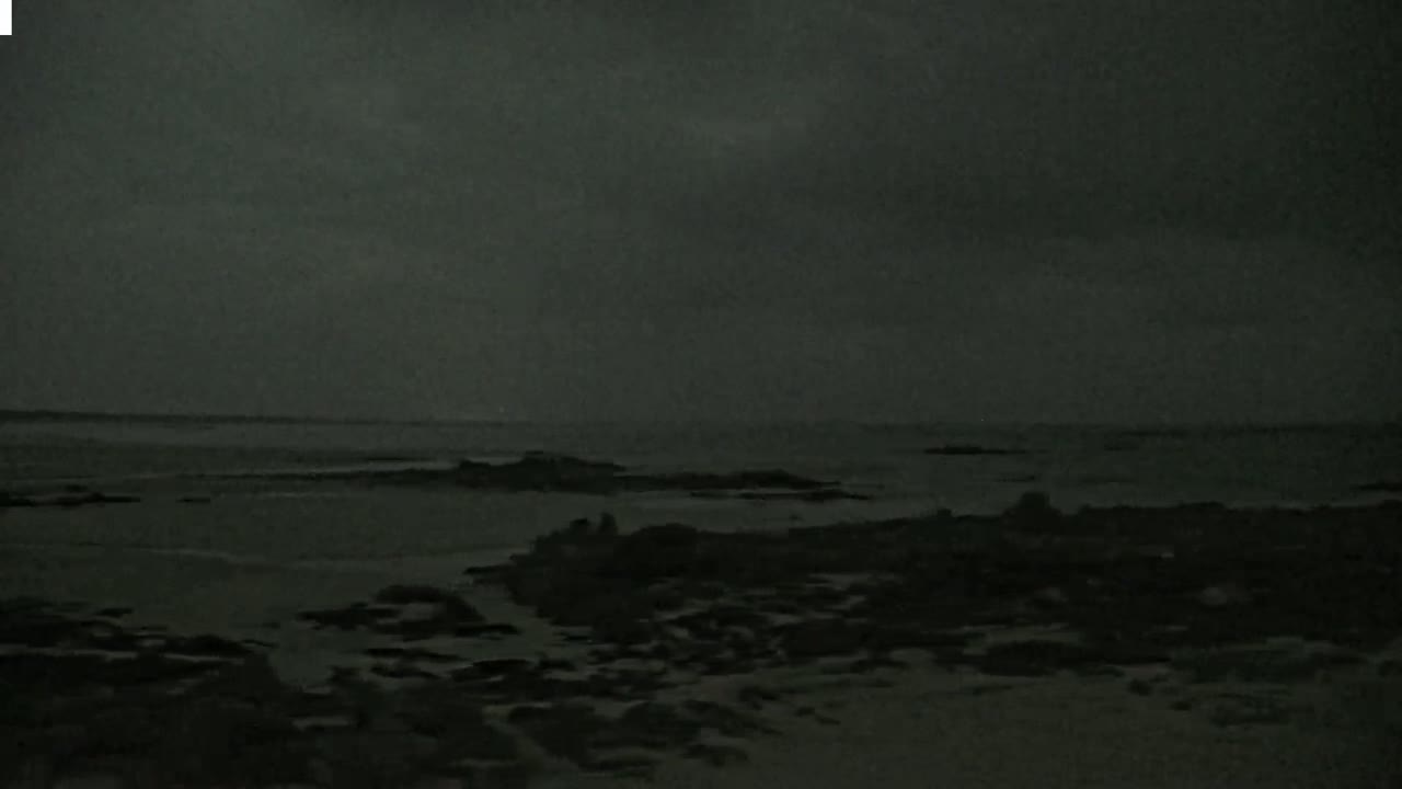 A dark, overcast sky hangs over a rocky shoreline and a calm sea at night.