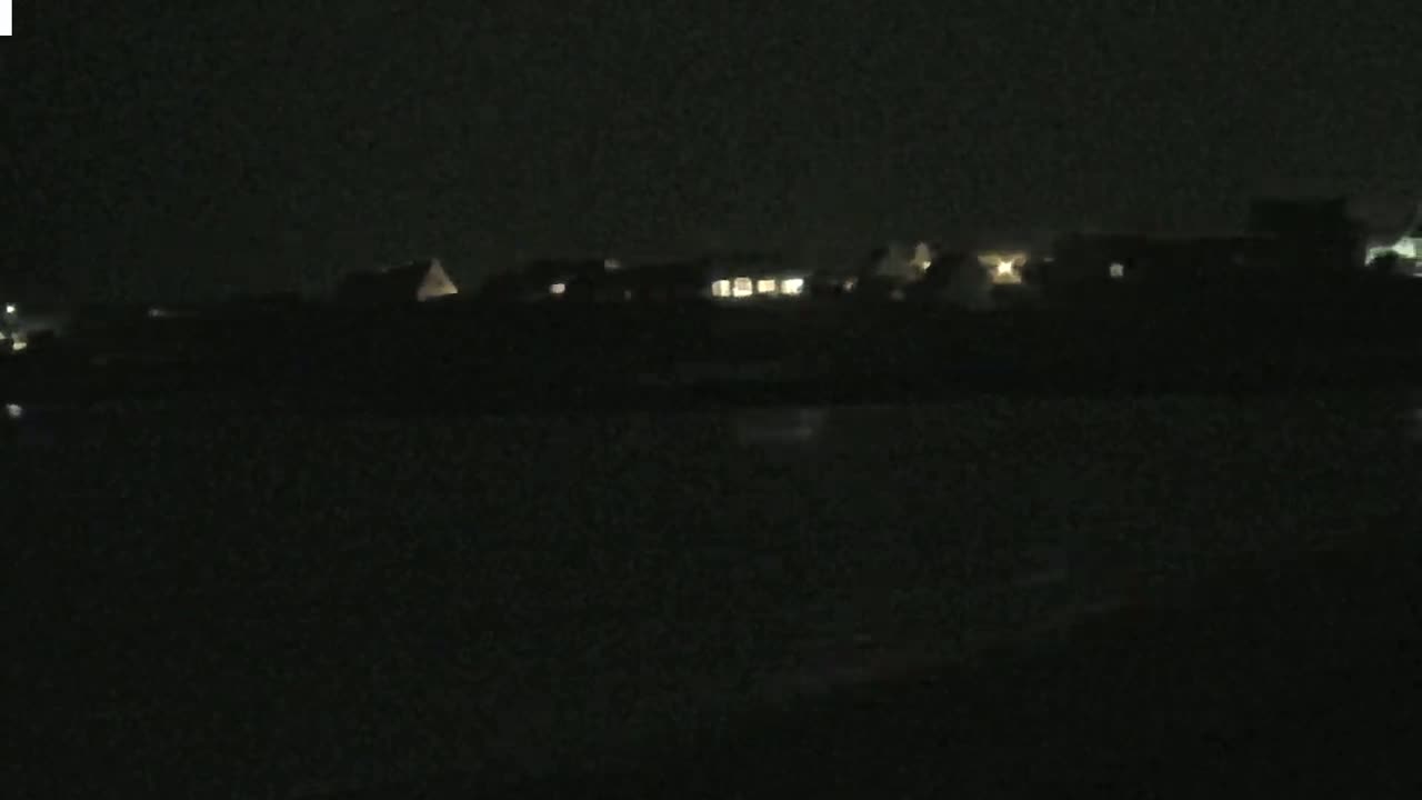 At night, faintly lit buildings are visible across a dark body of water.