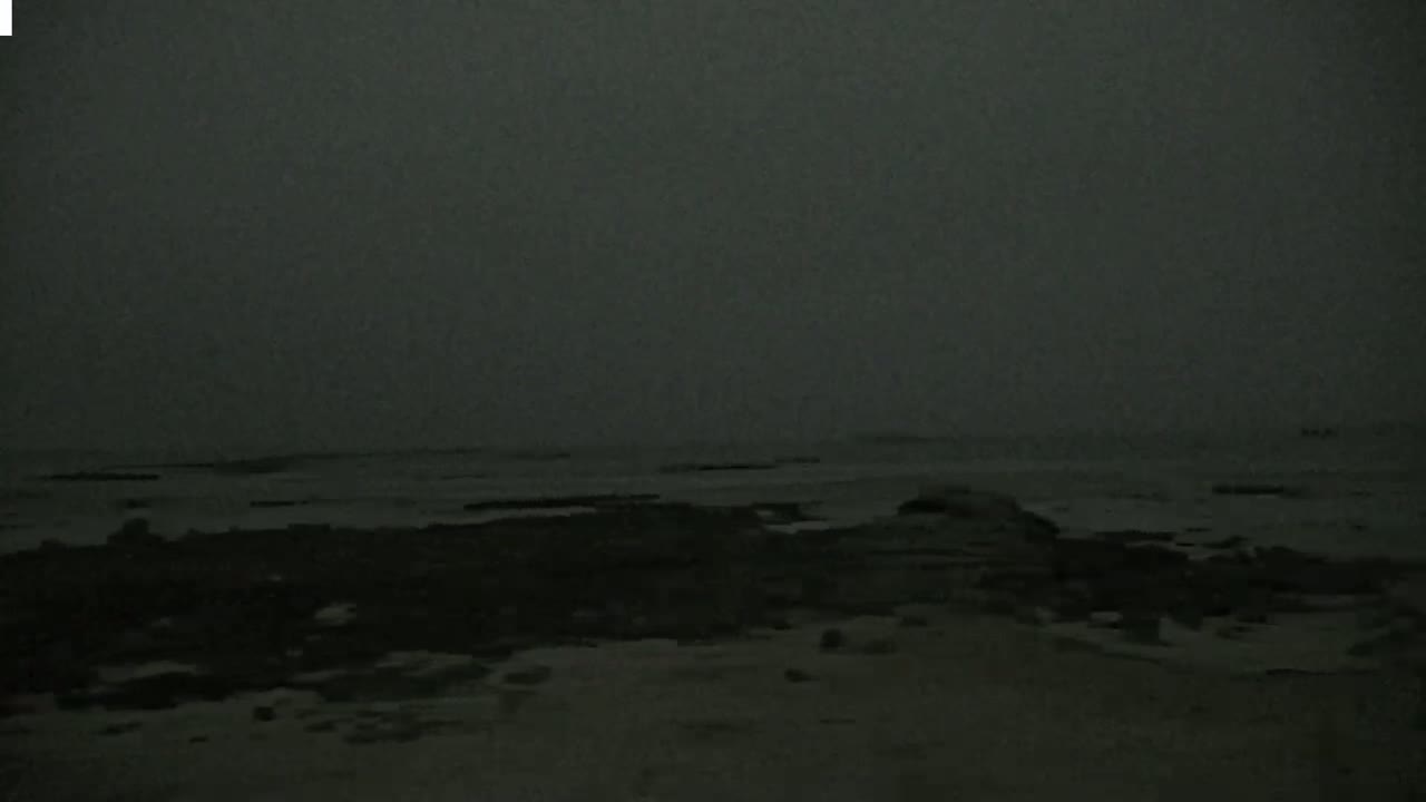 A dark, overcast sky hangs over a beach with dark, wet sand and rocks visible near the water's edge.