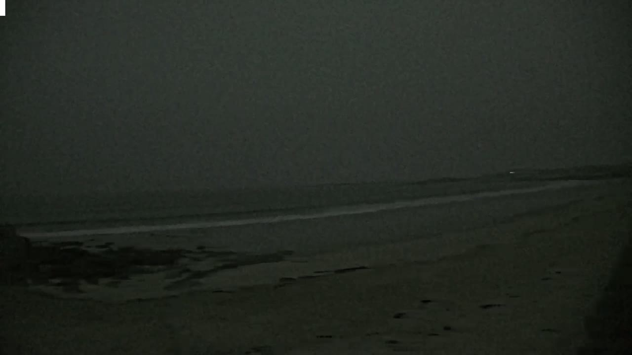 A dark, overcast sky hangs over a beach with a dimly lit ocean.