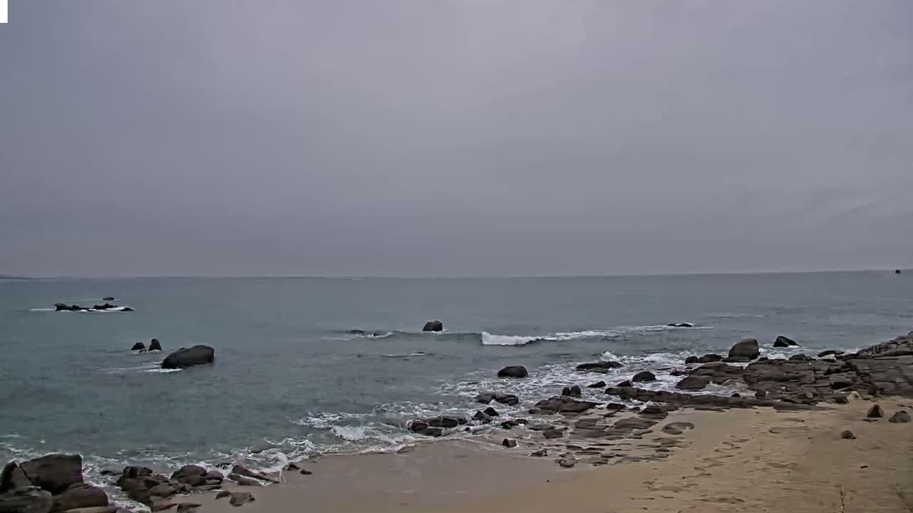A rocky shoreline with small waves under an overcast sky.