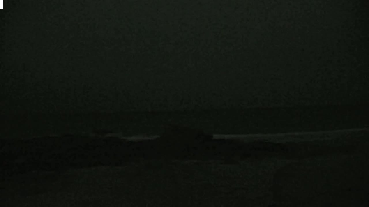 A dark, nighttime image shows a blurry, indistinct shoreline with dark water.