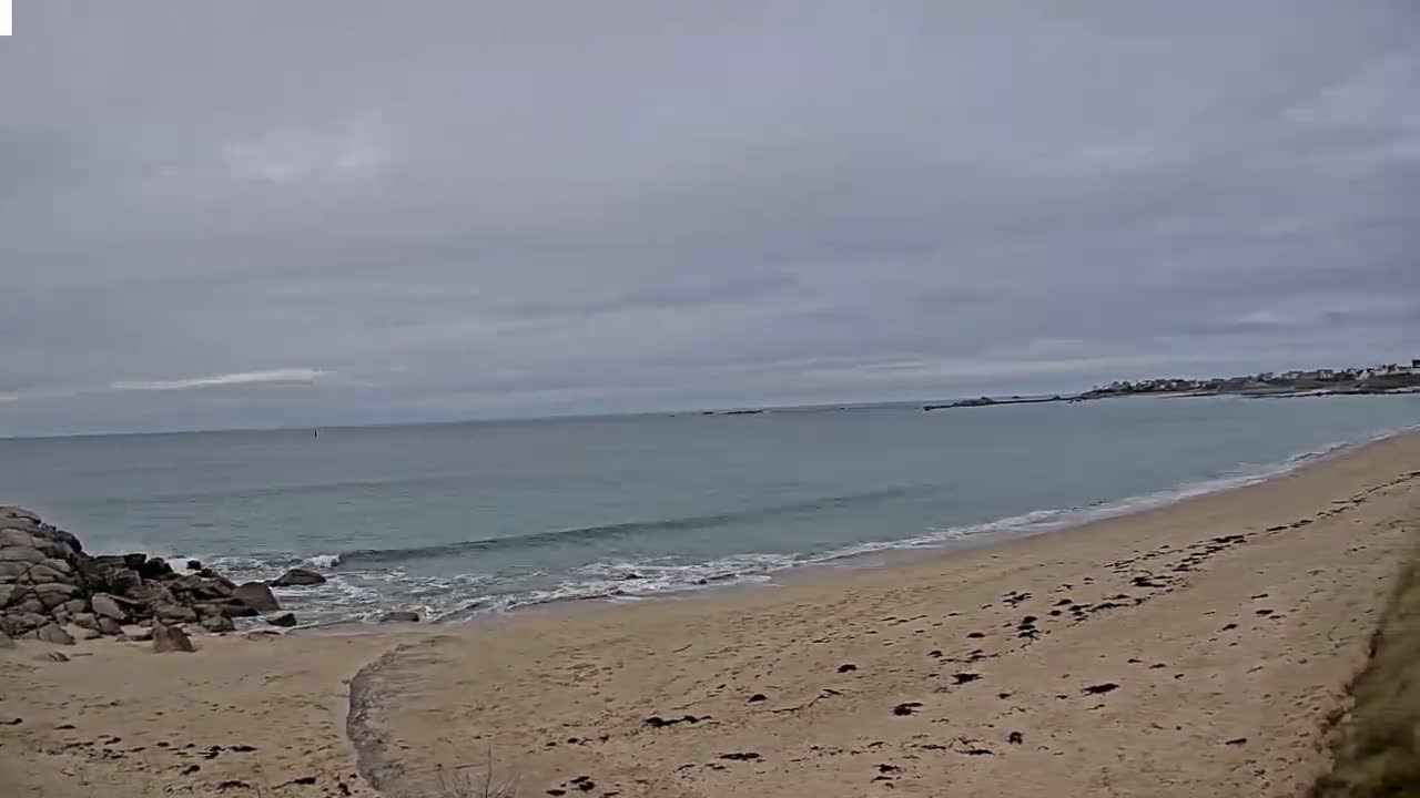 A sandy beach with small waves laps the shore under an overcast sky.