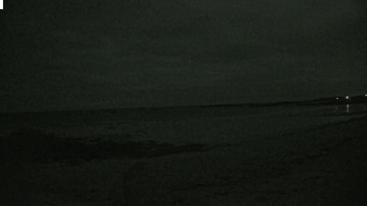 A dark, nighttime view of a calm body of water under an overcast sky.