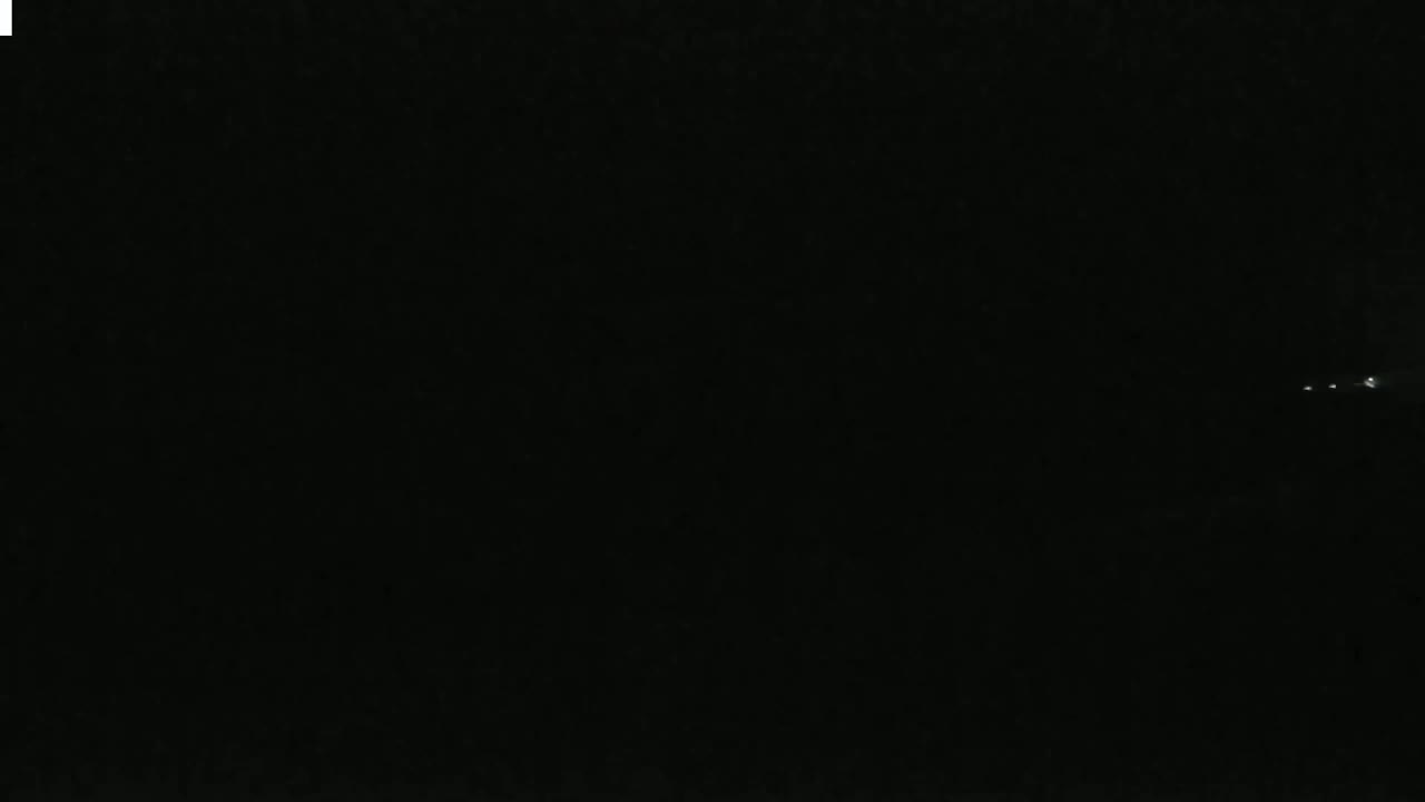 A nighttime image shows a few faint lights in the distance against a completely dark sky.