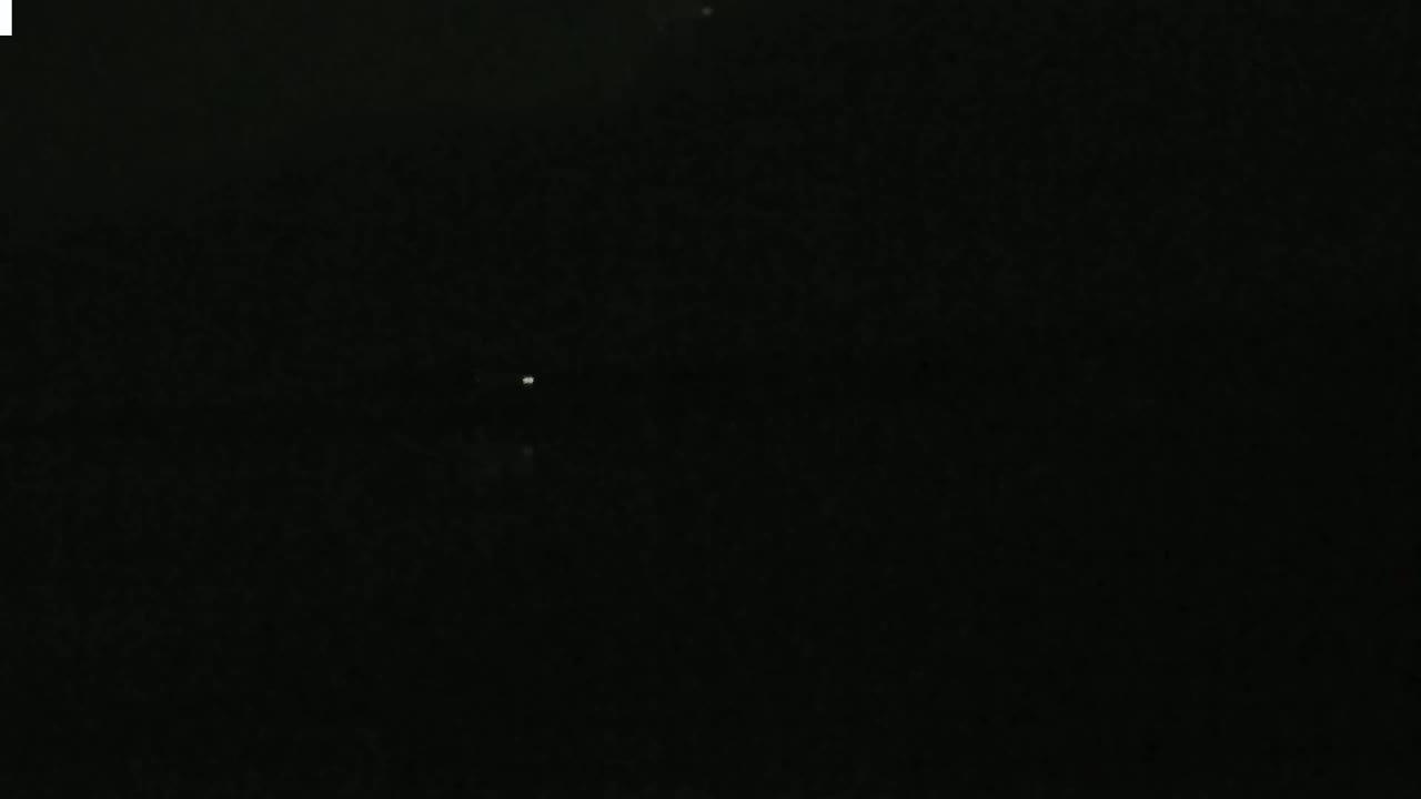 A very faint, small light is visible in a dark, nighttime sky.