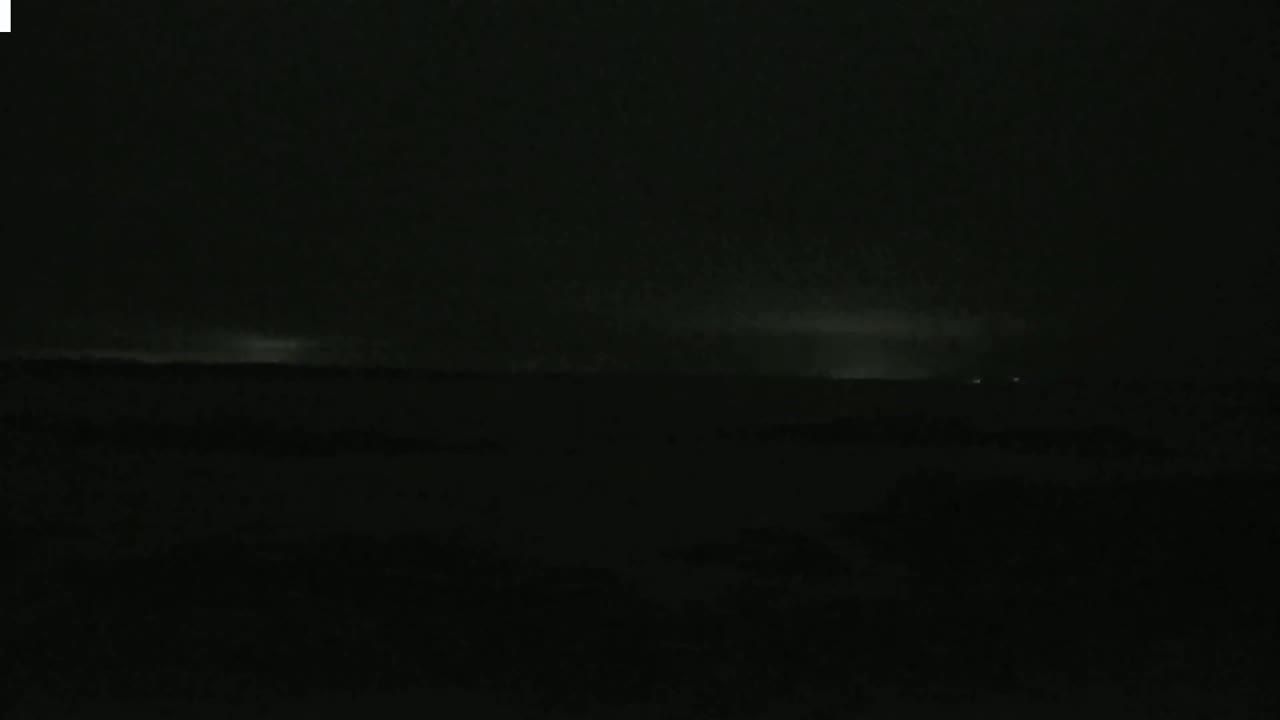 A dark, nighttime landscape shows distant lightning illuminating a low-lying cloud layer.