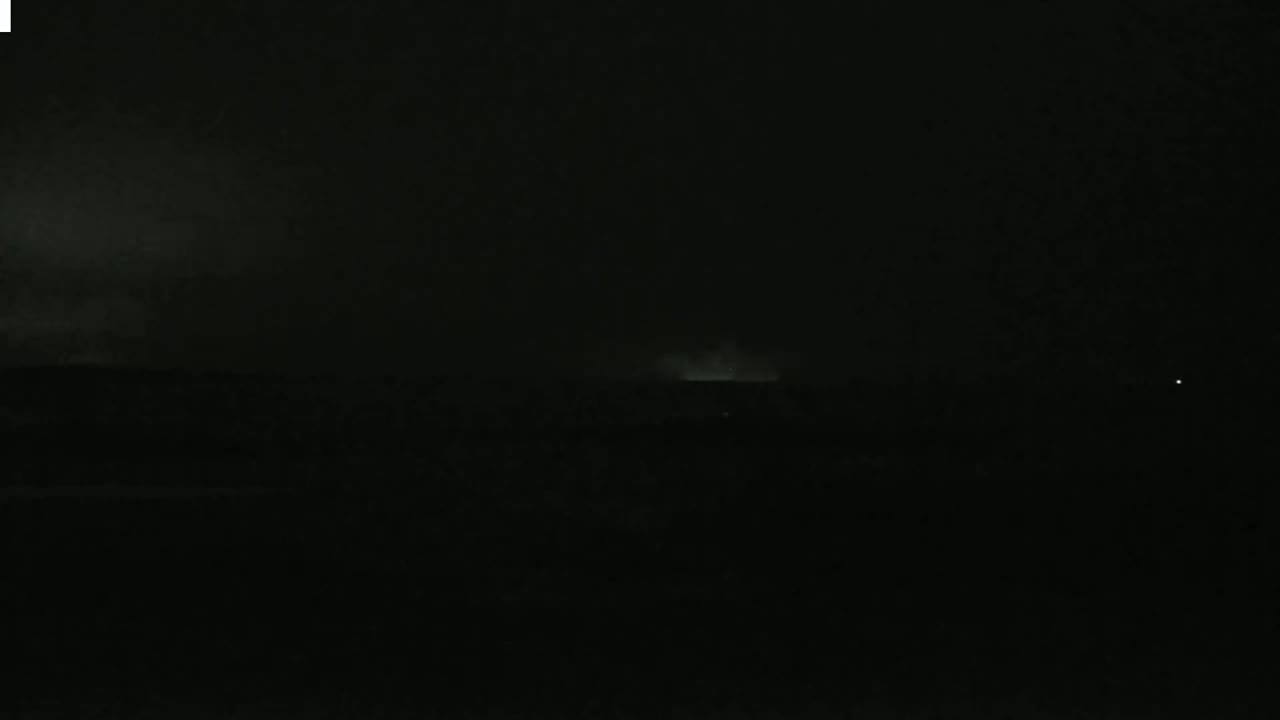 A dark, nighttime landscape with a faintly illuminated horizon possibly indicating a storm in the distance.