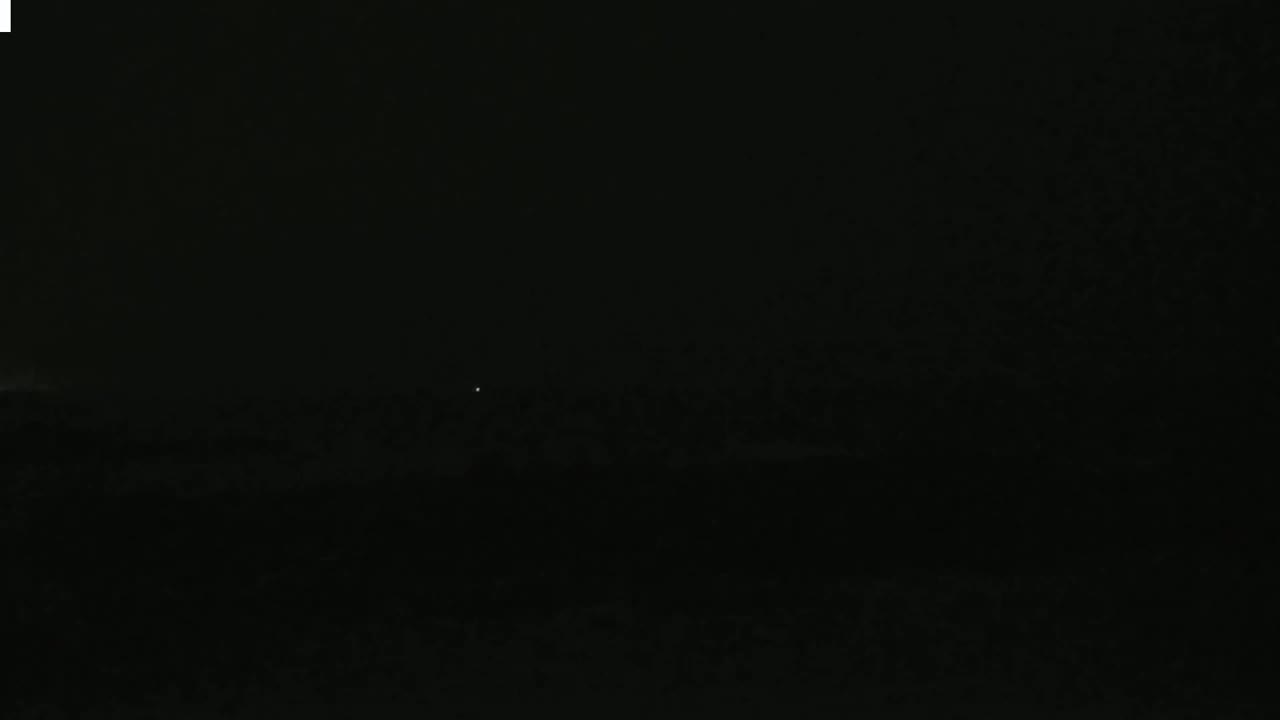 A dark, nighttime landscape is visible with a few faint lights in the distance.