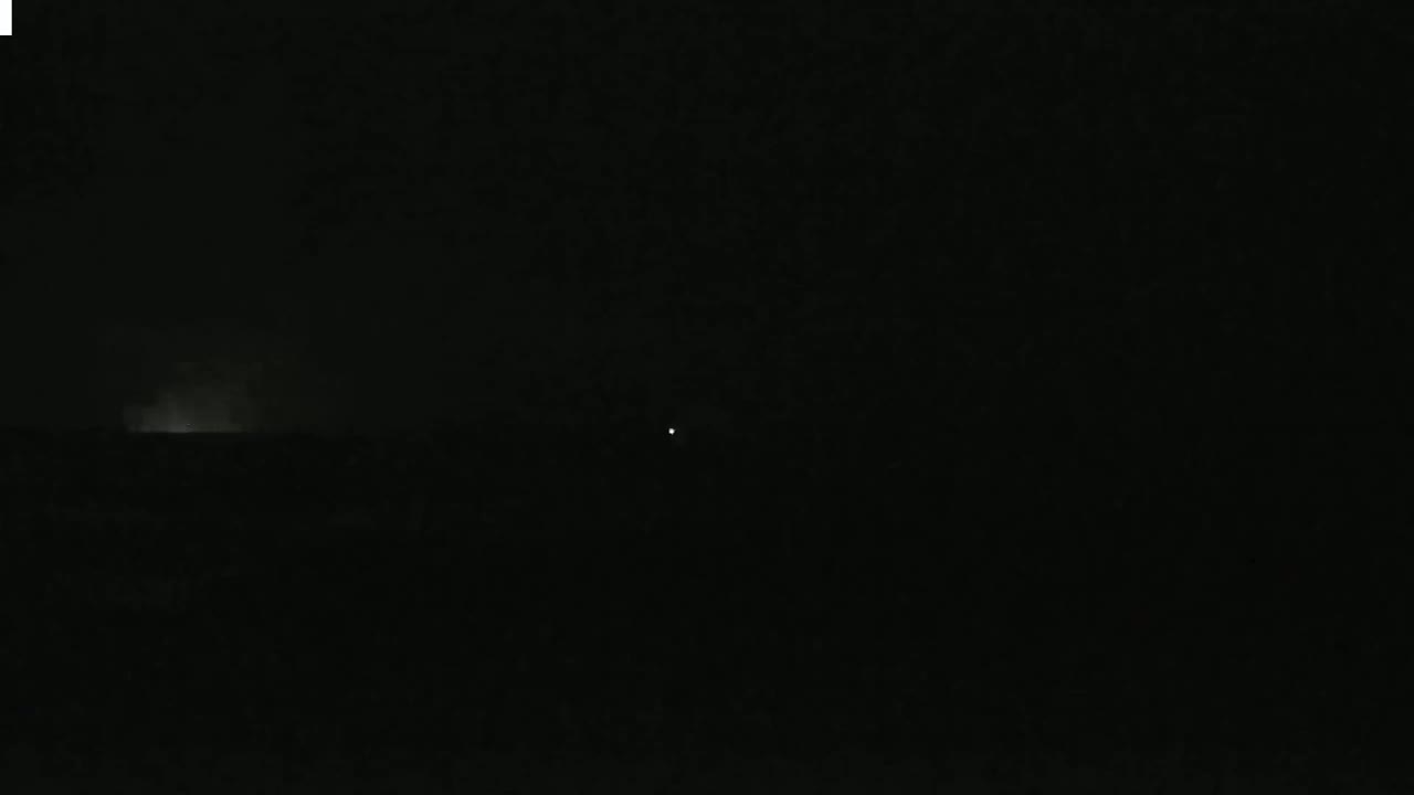 A dark, nighttime scene shows a faint, bright horizon line with a single, small light in the distance.