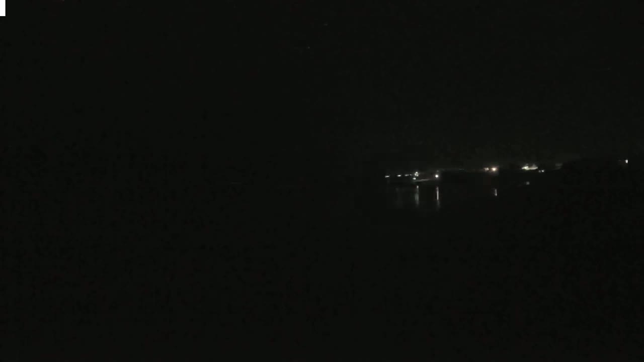 A dark, nighttime view of a body of water with faint lights visible in the distance on the opposite shore.