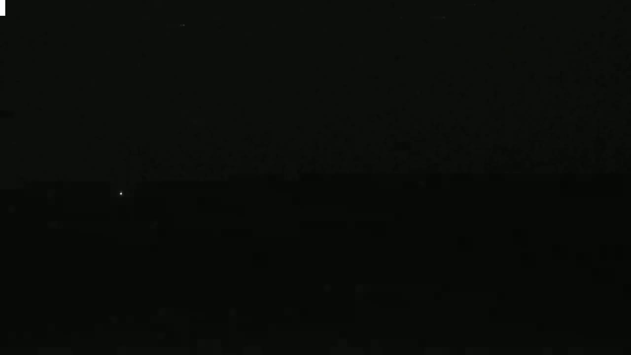 A single, faint light is visible in the distance on a dark, nighttime horizon.