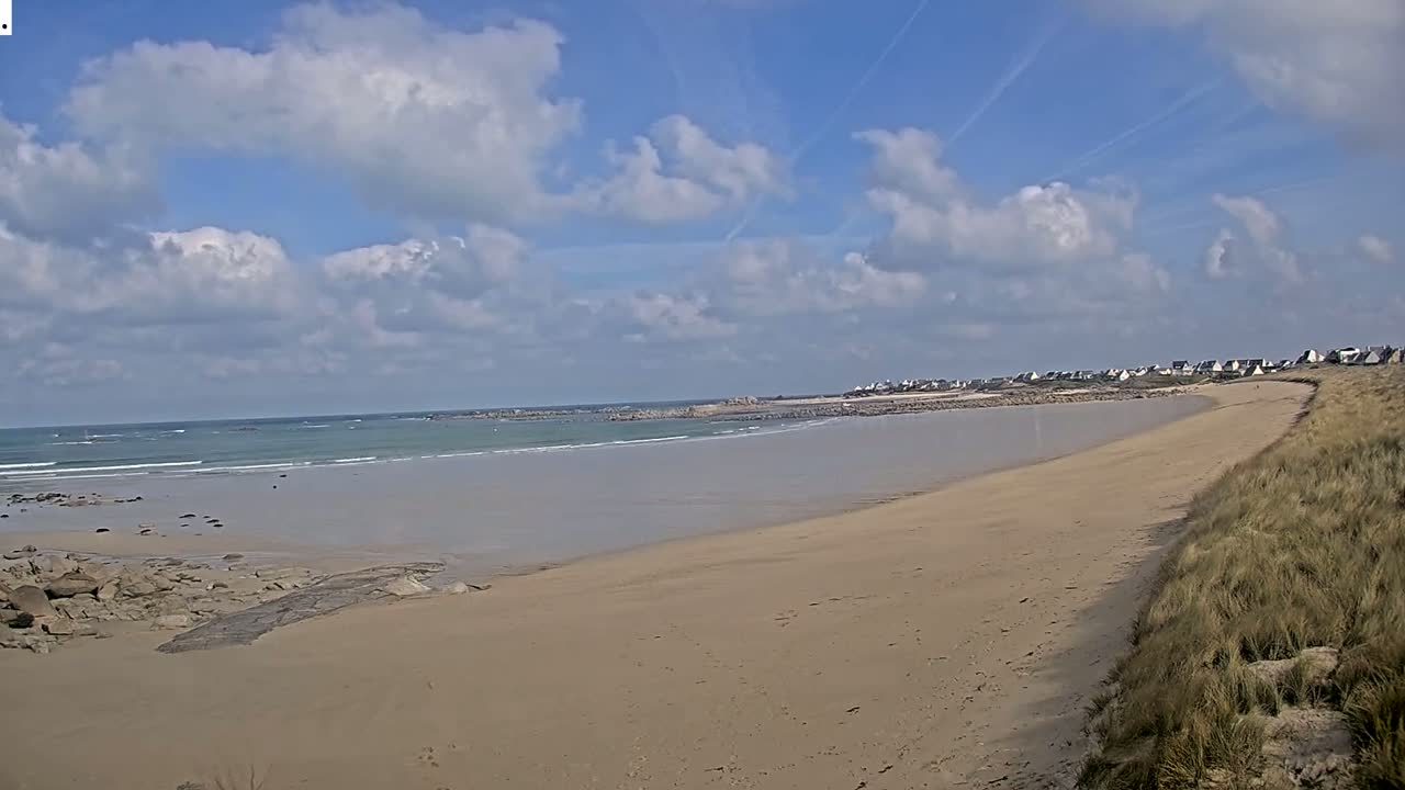 A sandy beach stretches to a calm ocean under a partly cloudy sky.