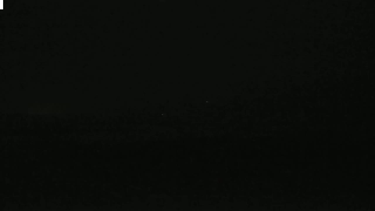 A very dark, nighttime image shows a few faint lights in the distance.
