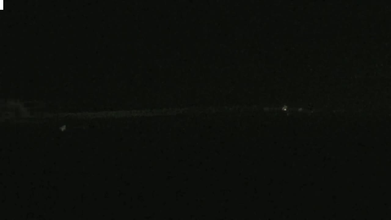 A faint, low-lying light source stretches across a dark, nighttime scene.