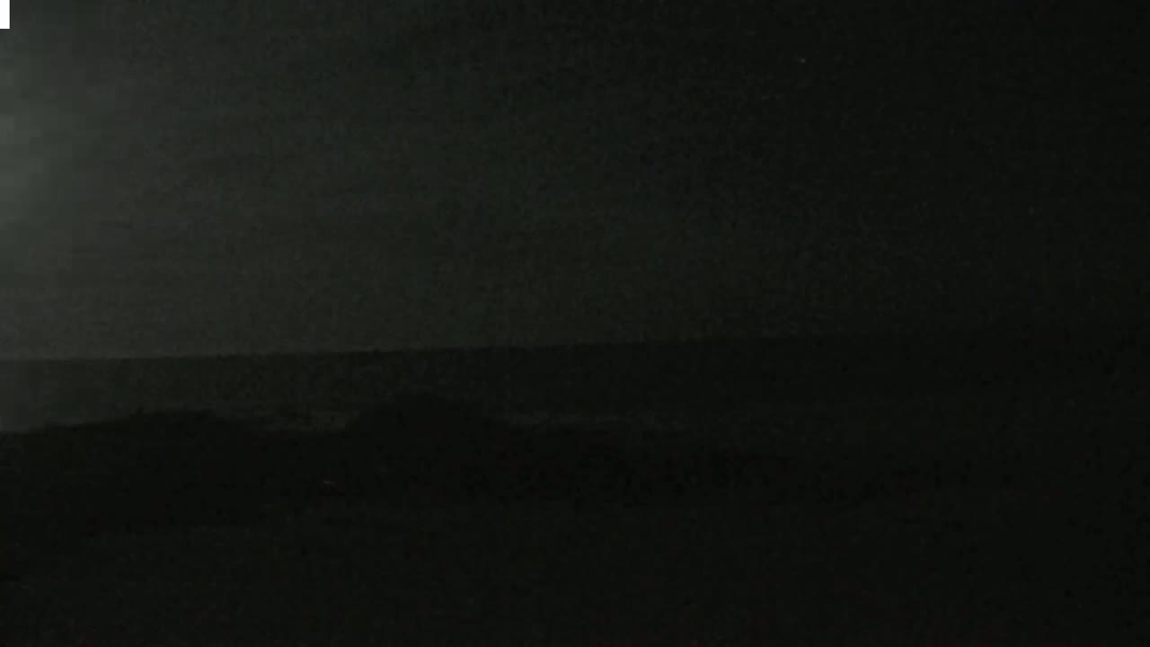 A dark, nighttime landscape shows a dimly lit horizon line separating the land from a dark sky.