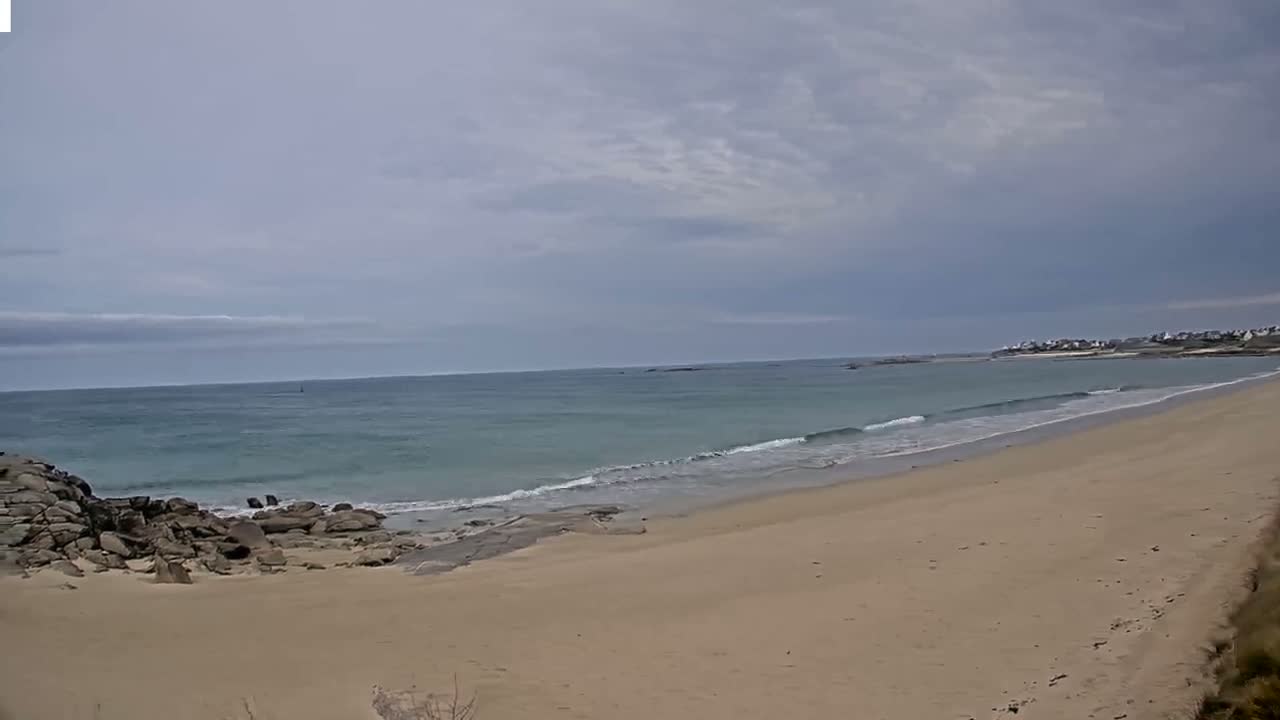 A sandy beach stretches out to a calm, light-blue ocean under a mostly cloudy sky.