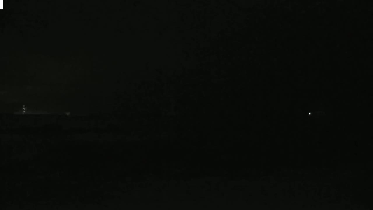 A dark, nighttime scene shows a few faint lights in the distance.