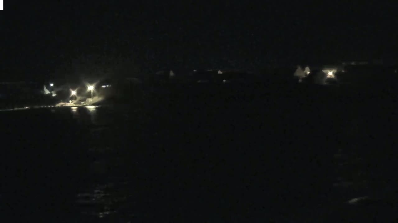 A dark, nighttime scene shows faintly lit buildings across a body of water.
