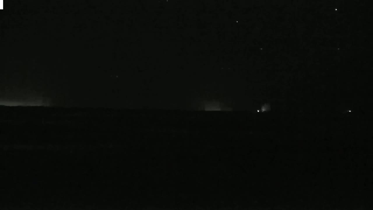 A dark, nighttime landscape with a faint, distant glow on the horizon and a few scattered lights.