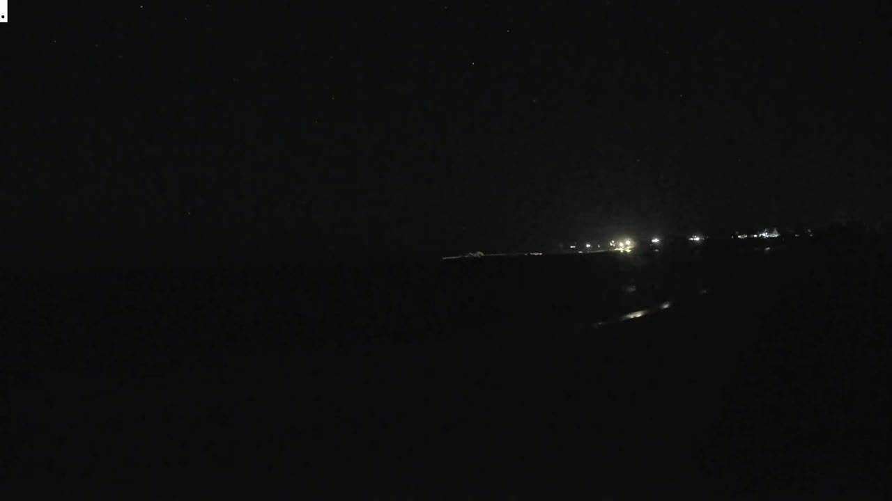 A dark, nighttime scene shows a distant line of faint lights on the horizon under a clear, starlit sky.