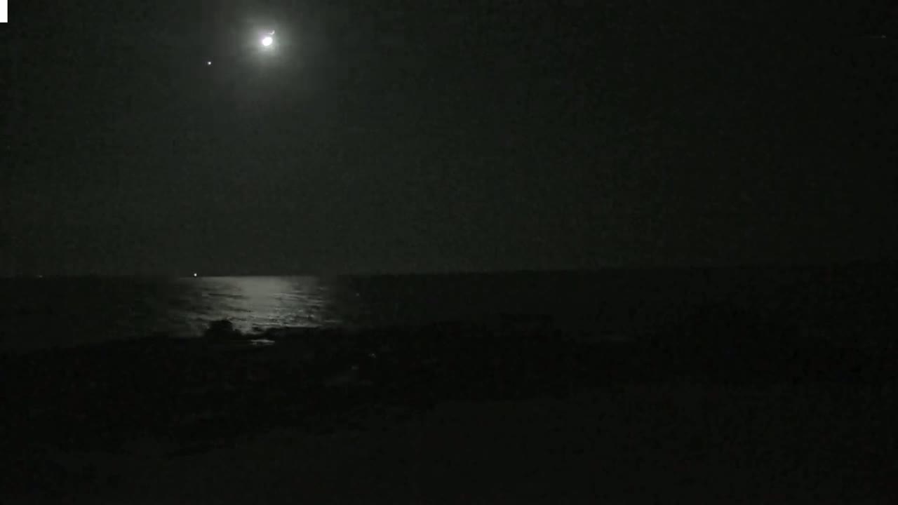 A bright moon illuminates a dark, calm ocean at night.