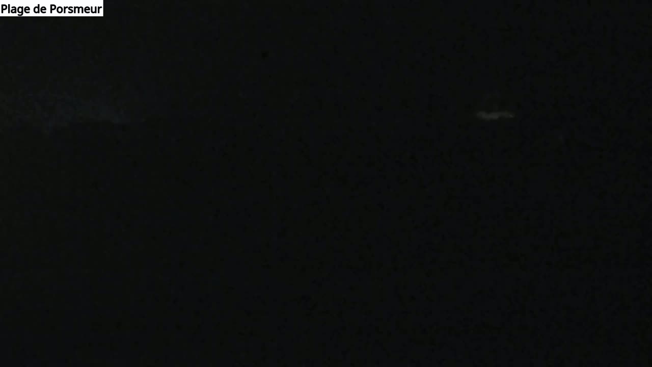 A very dark image shows a dimly lit, possibly nighttime scene with faint light sources in the distance.