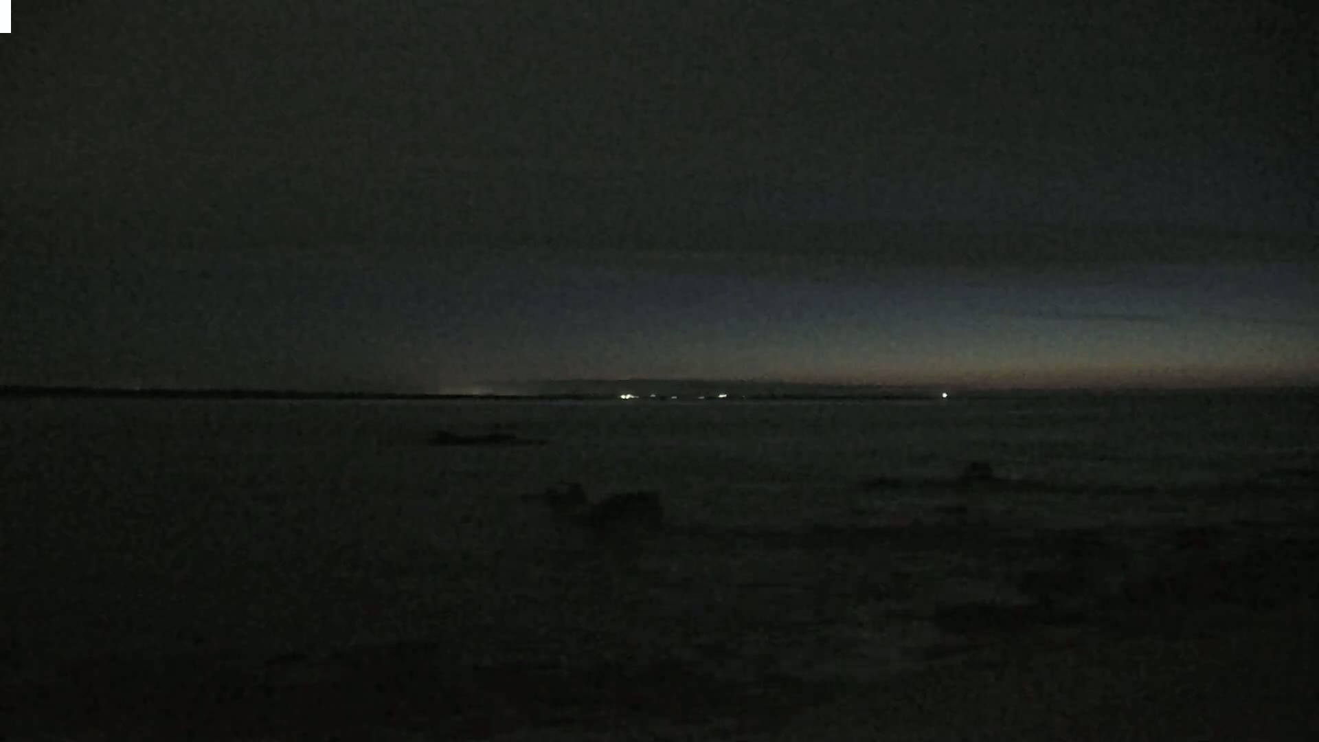 A dark, still body of water is shown at night with a faint, dusky light on the horizon.