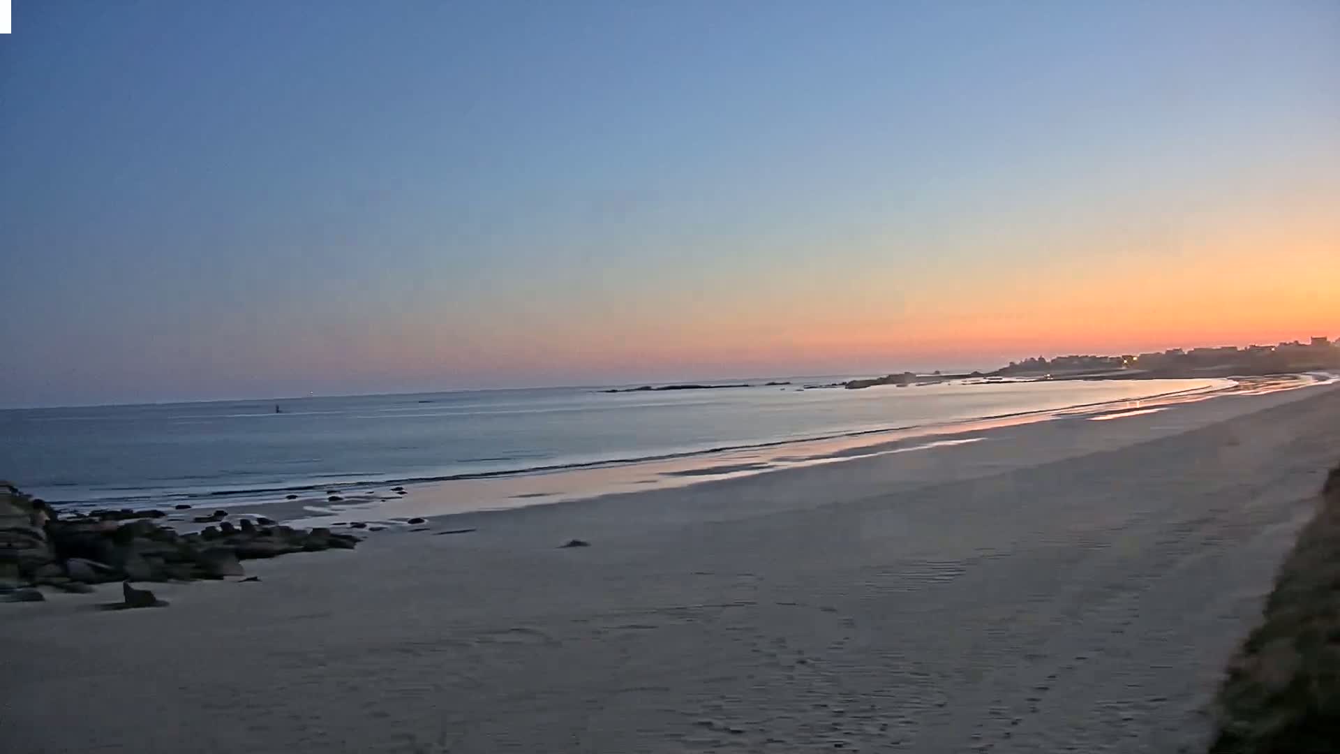 A sandy beach stretches to a calm ocean under a sunset sky.
