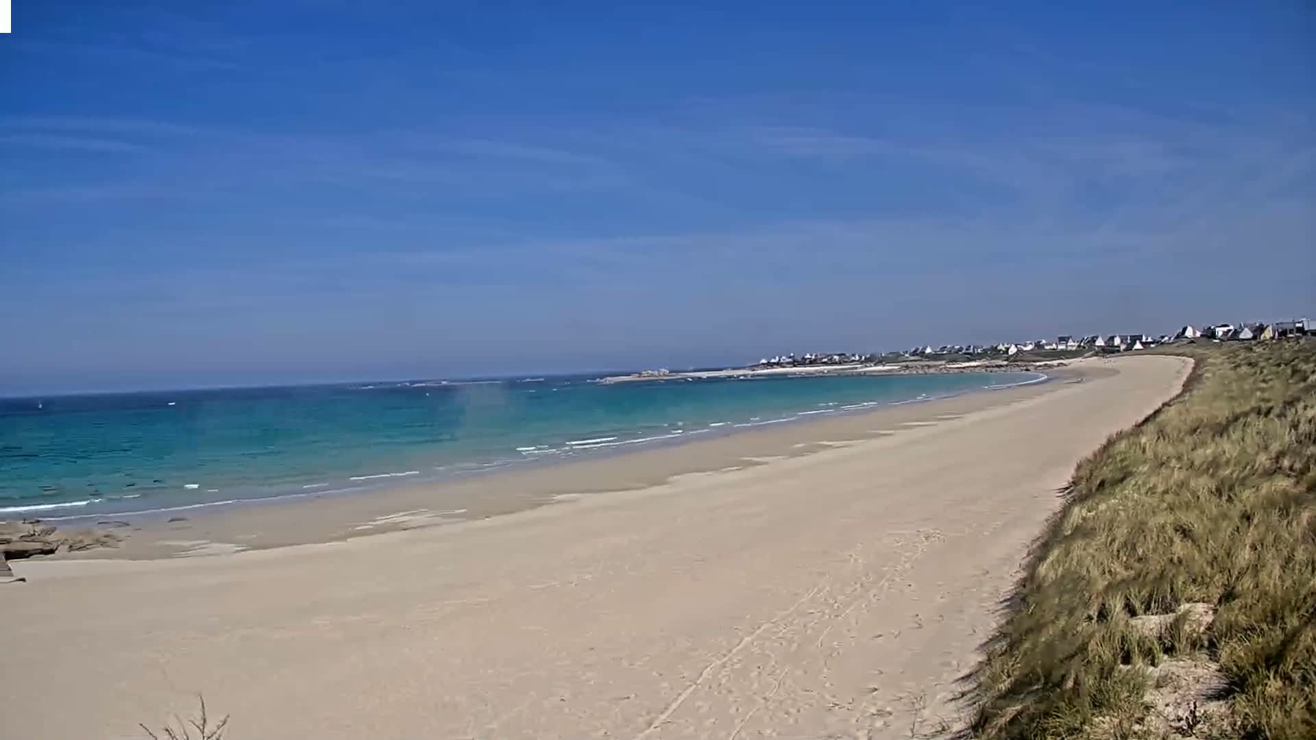 A long, sandy beach curves gently to the left, meeting a calm, turquoise ocean under a clear blue sky.