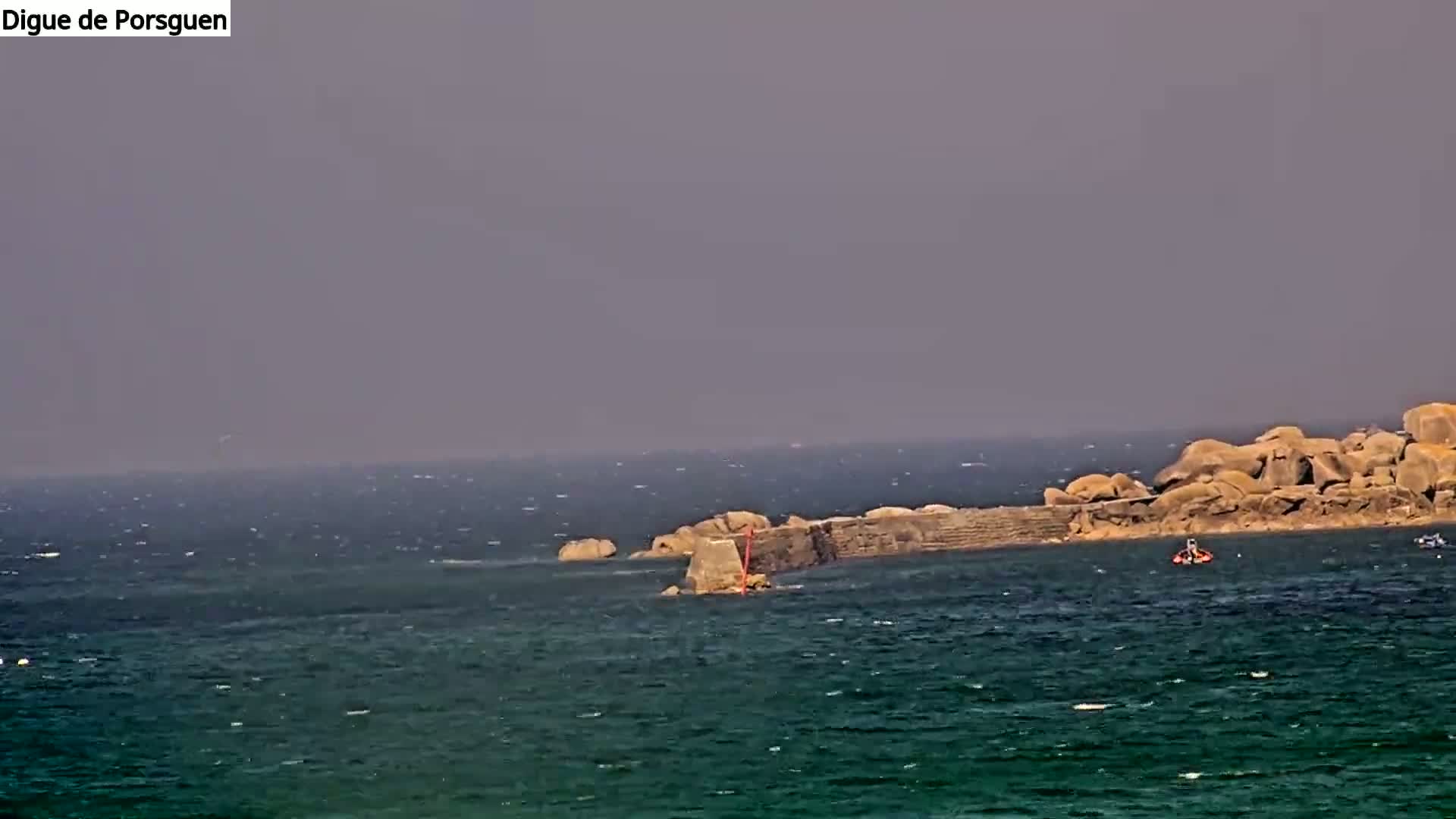 A rocky outcropping with a low wall extends into a choppy sea under a hazy sky.
