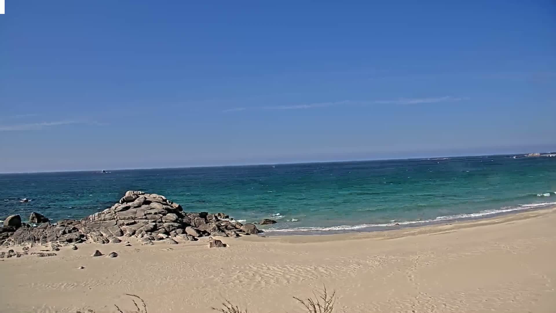 A sandy beach meets a teal ocean under a clear blue sky.