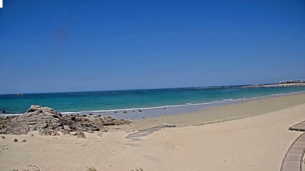 A sandy beach with turquoise water under a clear blue sky stretches to a distant shoreline.
