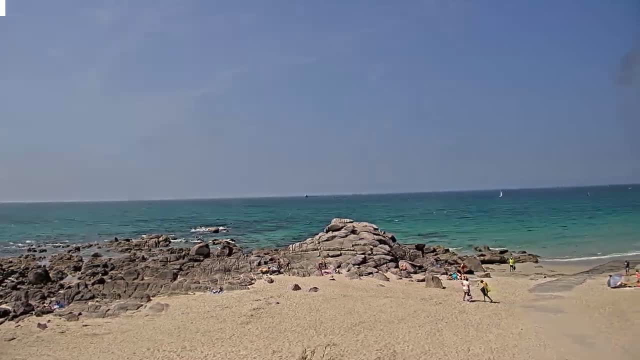 A sandy beach with rocky outcrops and a calm, turquoise ocean under a clear blue sky.