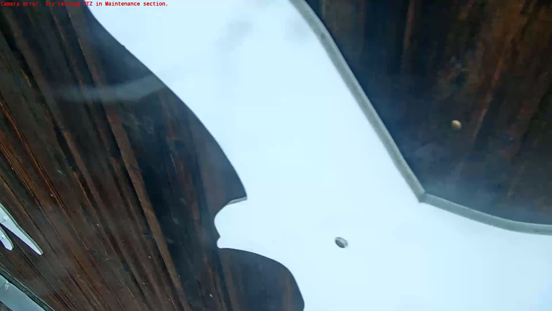 A low-angle, close-up view shows a large white object, possibly a sign or piece of artwork, partially obscuring a dark wooden surface outdoors in what appears to be overcast weather.
