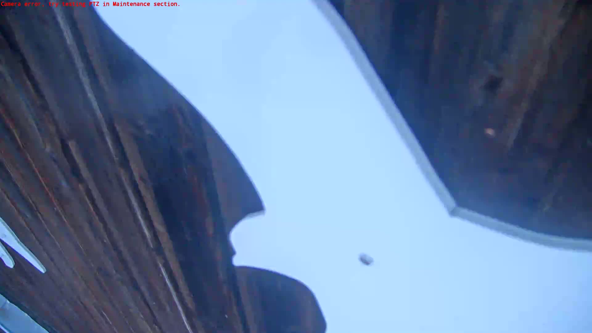 A low-angle view shows a dark, wood-paneled surface angled upward against a pale blue sky.