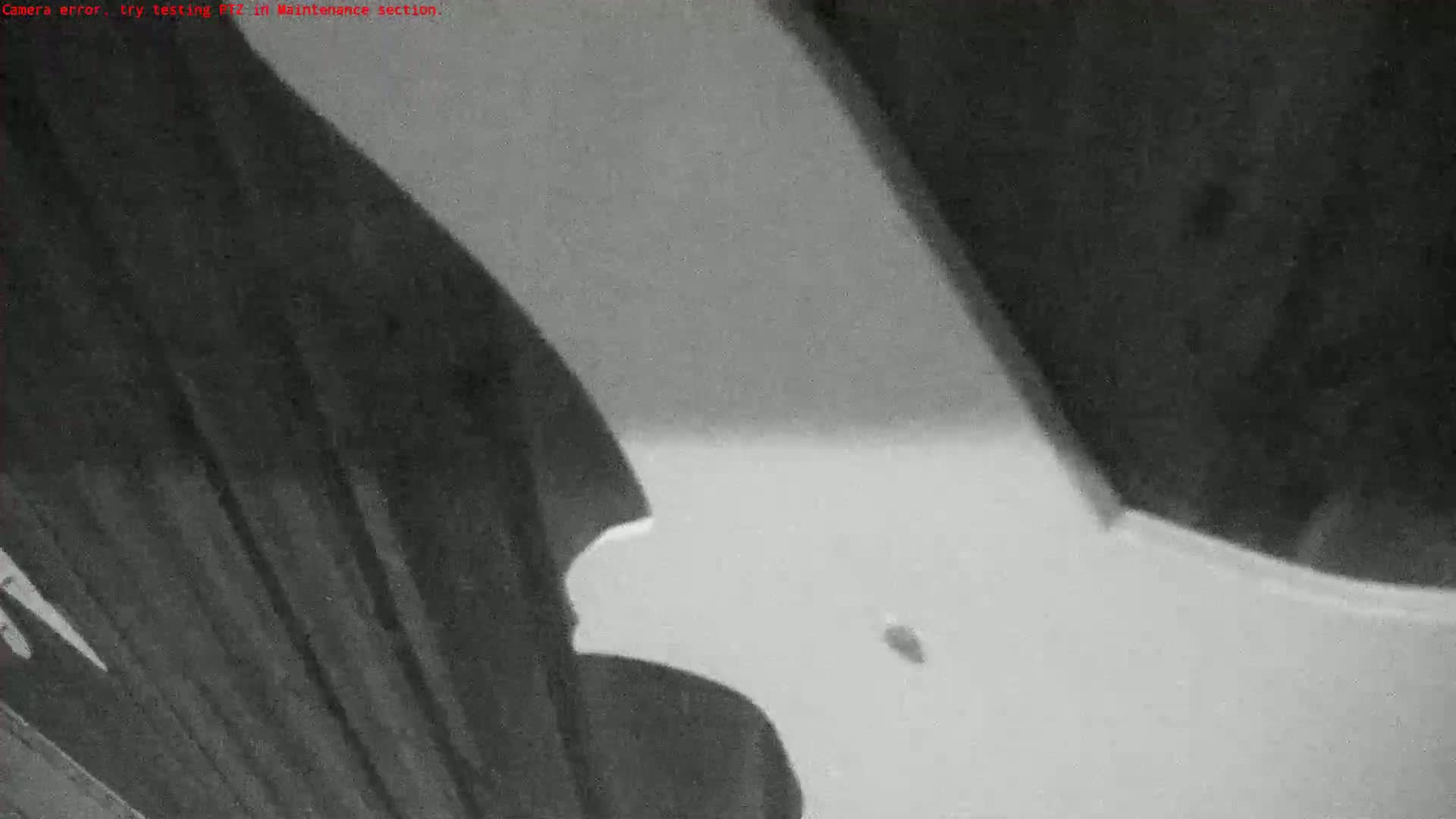 A grainy, low-light image shows a large, light-colored object, possibly made of plastic or metal, angled against a dark, textured background.