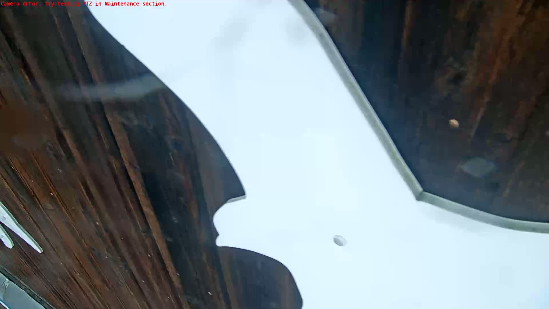 A low-angle view shows a large white shape, possibly part of a building's exterior, against a dark brown wooden background.